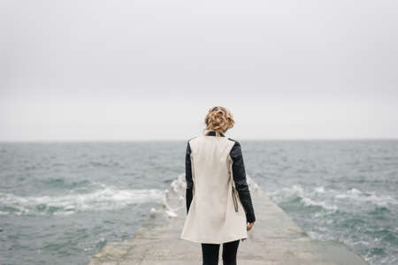 The beautiful girl stands with her back on the pier and looks at the sea.の写真素材