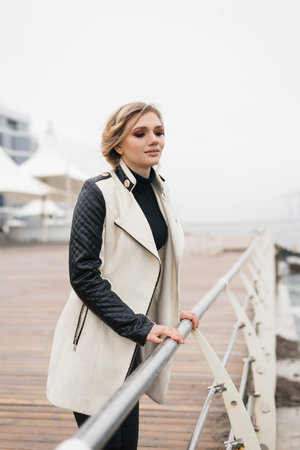 Slightly alarmed and a little sad girl walks by the sea. She holds onto the metal fence of the pavement and looks anxiously forward.の写真素材