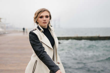 Cute smiling girl is walking along the waterfront. She raised her right hand to her temple, as if surprised by something.の写真素材