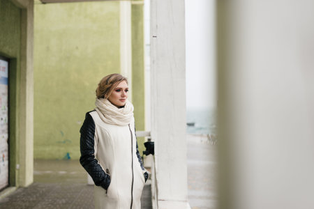 a nice and beautiful girl stands near a light column and looks thoughtfully into the distance