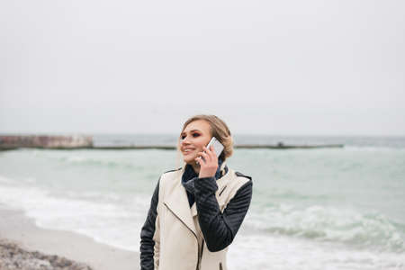 beautiful girl stands on the beach, talking on the phone and cute smilingの写真素材