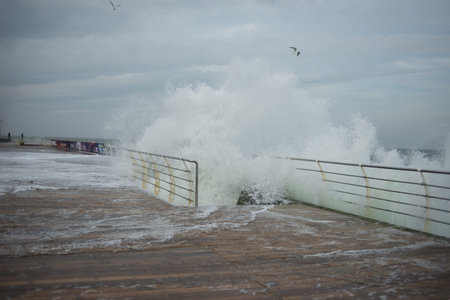 huge waves cover the pier during a storm, gulls fly from aboveの写真素材