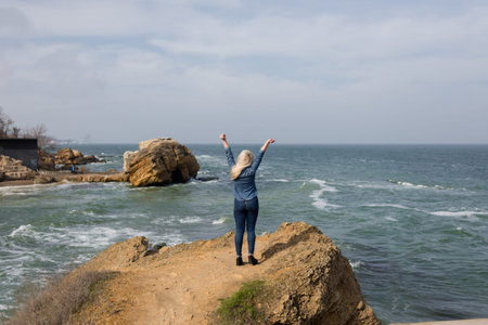 the girl is standing over a rock over the sea and raised her hands upwards
