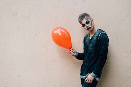 A guy with white skin holds an orange balloon in his hands and smiles into the cameraの写真素材