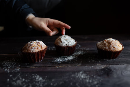 cupcake without cream on a wooden table with a place for the text. A hand reaches for one of the...