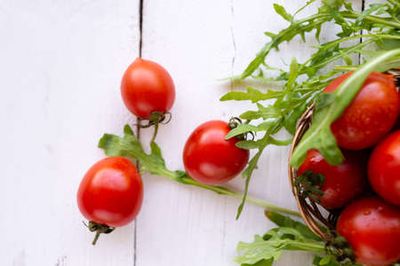 Some ripe and red cherry tomatoes lie on a wood table. Nearby are the leaves of arugula. Ripe and healthy foodの写真素材