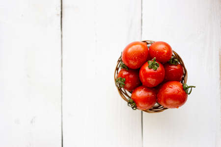 A few small and tasty cherry tomatoes lie in a basket on a wooden table. There is a place under the textの写真素材