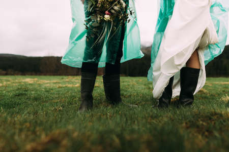 the feet of a man and woman are wearing rubber boots. They stand outside in the rain. Cold wind and moistureの写真素材