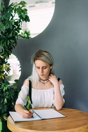 girl sits in a cafe at a table makes notes in a notebook.の写真素材