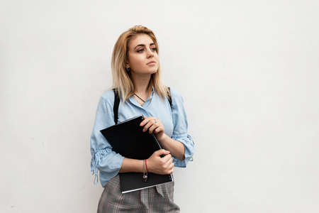 student holds a magazine and a backpack against the background of a white wall. girl goes to lecture.の写真素材