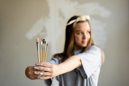 The girl thinks over the picture on the wall. In the hands of holding brushes of different sizes and...