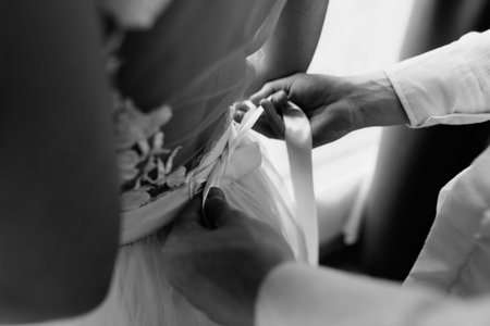 black and white close-up photo, the groom helps the bride to dress the wedding dress, the husband will tie a bow on the dressの写真素材
