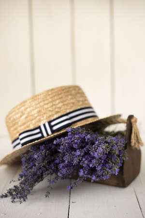 on a white background there is a wooden basket with a fragrant fresh bouquet of olive lavender on it lies a charming hat.の写真素材