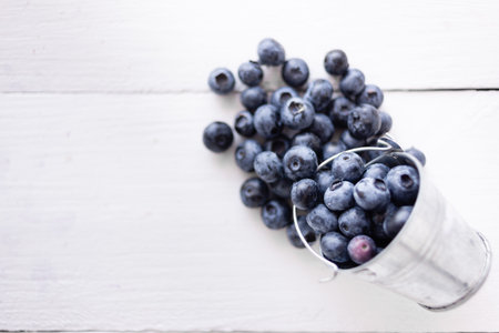 A bucket full of freshly picked blueberries on a white wooden table. Delicious healthy berries