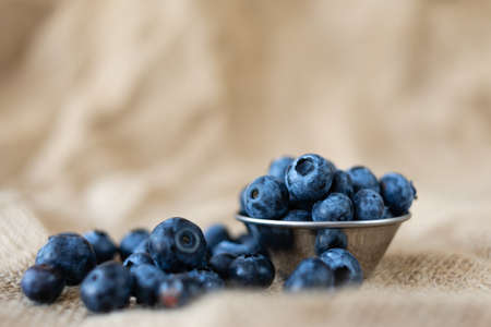 Fresh organic blueberries in a plate of metal on burlap cloth on a rustic wooden table. Healthy food, vegan diet or raw food concept.の写真素材