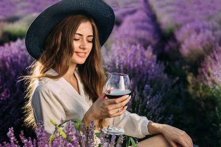 girl sitting in a field with lavender, a glass of wine in a female hand. Camping, wonderful lifeの写真素材