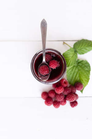 top view, ripe berries of raspberry lie on a white table. Glass jar of jamの写真素材