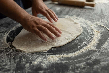 The chef in the kitchen rolls out the pizza dough. Male hands of a baker. The process of cookingの写真素材