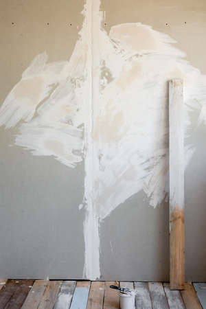 grouting the plasterboard wall. structural grouting is applied on the wall. on the floor is a bucket with white putty and painted board.の写真素材