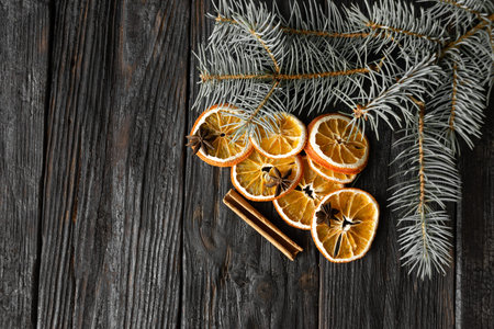 dry sliced orange with a cinnamon stick and a sprig of spruce on a black board. Place for an...