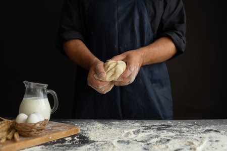 male chef hands knead the dough in a working apron on a black background