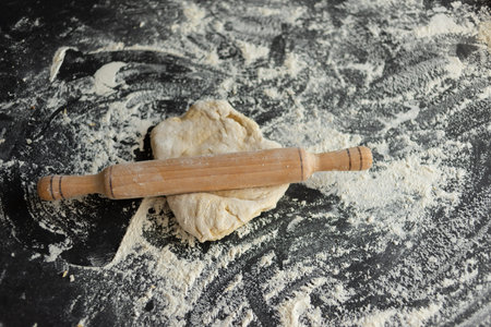 Rolled dough with rolling pin on wooden table covered with baking flour. Pizza cooking background.