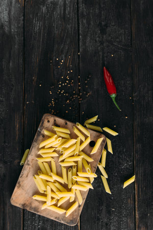 raw pasta lie on the kitchen board, hot hot peppers, wood background, ingredients for preparing a delicious meal. Place under your text.の写真素材