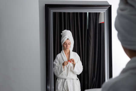 a girl in a white coat stands in front of the mirror, opens a cosmetic napkin. cleaning procedure. preparing the face for applying the cream.の写真素材