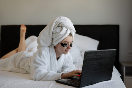 girl freelancer lying on the bed working on a laptop. free work schedule. woman blogger prints text.の写真素材