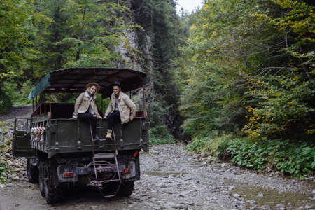 Photo of a man and a woman who are sitting in an open truck on a background of trees and mountains. Portrait of travelersの写真素材