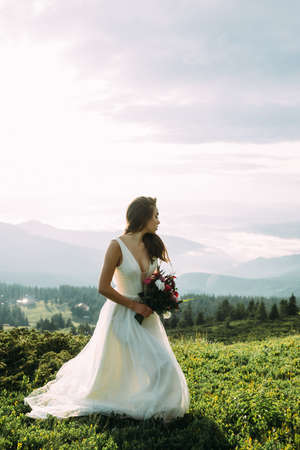 Bride with bouquet stands on a green hillの写真素材