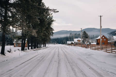 Snow road along the village, ahead of a beautiful view of the mountain hillsの写真素材