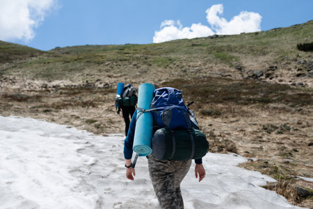 Tourist with a backpack walks on a snowdrift in the mountains, view from the back