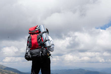 Tourist with a large backpack stands on hill and looks skyの写真素材