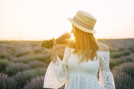 Beautiful brunette with a white dress and a straw hat posing with a bouquet of lavender. Provence,...
