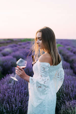 girl on a picnic, standing on a lavender field in her hand holding a glass of red wine.の写真素材