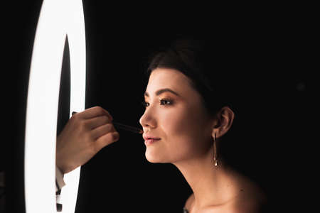 Makeup artist paints lips of a beautiful brunette. Makeup artist uses a ring lamp. Beauty Studioの写真素材