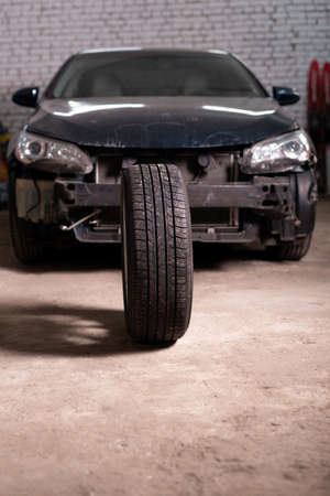 Photo of a car tire tire on the background of a passenger car without a bumperの写真素材