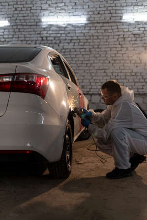 auto mechanic fixing the door of a white foreign car using a round grinding machine, sparks fly from the deviceの写真素材