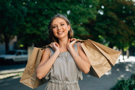Beautiful styled girl is surrounded by many packets of bought clothing. She is standing and holding...