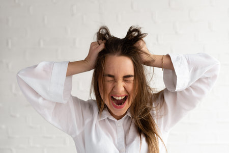 Portrait of frustrated irritated woman standing with hands at her head and screaming isolated over...