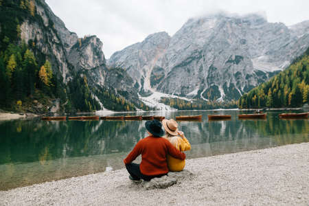 couple in love man and woman are sitting on the shore of lake lago di braies in Italy. men's and women's clothing. Quiet look of water. Rest of tourists. Place for textの写真素材