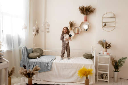 joyful girl plays in the children's room on the bed with her favorite toys. the child is standing on a baby bed and holding toys in his hands.の写真素材