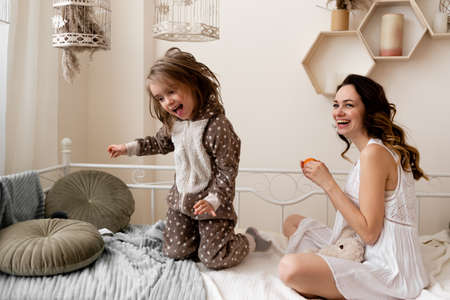 the child is jumping on the bed glad that she will be treated to a delicious mandarin duck. healthy vitamins for the baby. mom pleases her daughter.の写真素材