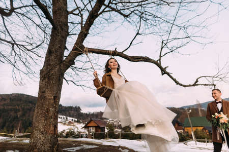 a cheerful and cheerful bride sways on a swing, laughs merrily and enjoys life. Stylish couple in love.の写真素材