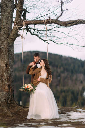 the young groom holds in his arms his beautiful bride against the backdrop of winter mountains.の写真素材