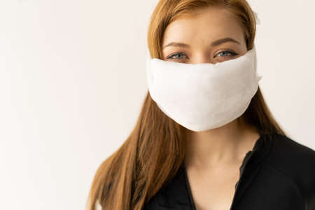 Beautiful caucasian young woman in a black t-shirt with a protective mask on her face. Protection against viruses and infections. Studio portrait, concept with white background. place for text. Do it yourself virus conceptの写真素材