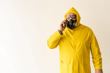 a man dressed in a yellow protective suit communicates on a cell phone. The concept of quarantine protection from the whole worldの写真素材