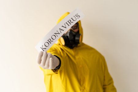 A man wearing a chemical protective suit on a light gray background. Hold in hand a sheet with the...