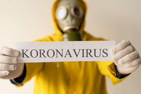 A man in yellow Hazmat suits and a gas mask holds an inscription with the text Coronavirus, gray background. Place for textの写真素材